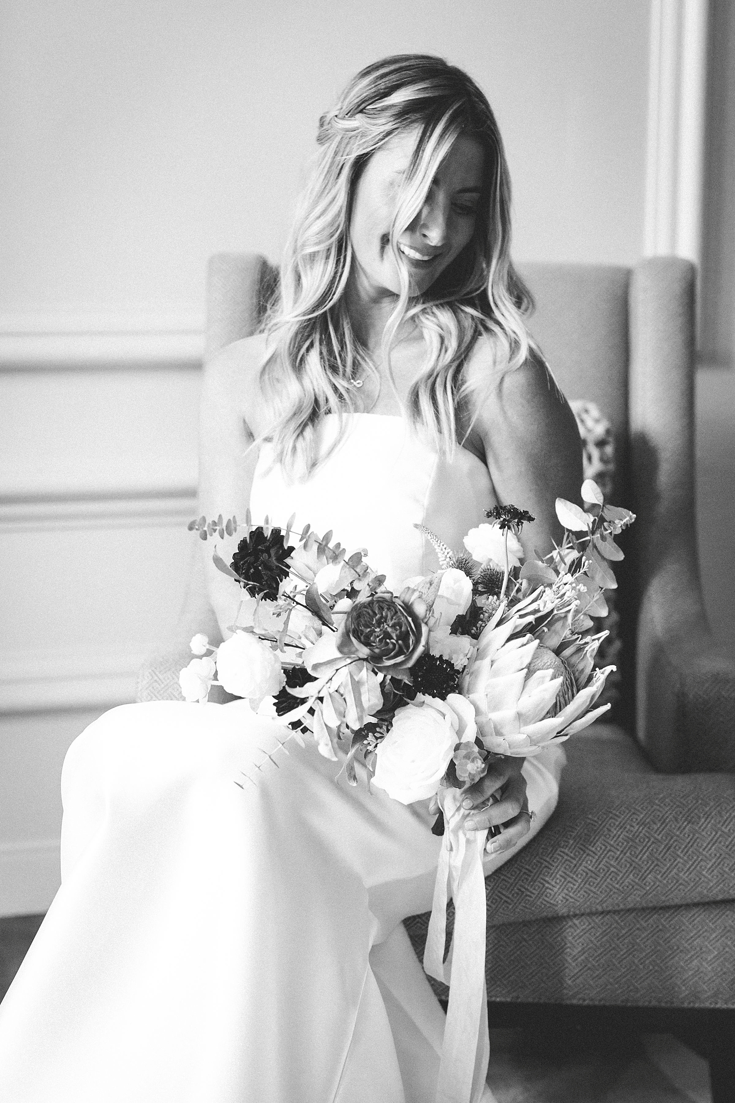Black and white photo of a bride on a chair holding a bouquet